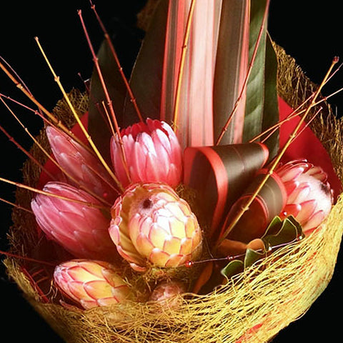 A contemporary design of proteas and decorative wooded stems are wrapped in a naturalistic weave.