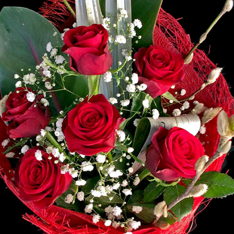 A classic bouquet with six beautifully wrapped red roses garnished with greenery and a light spray.