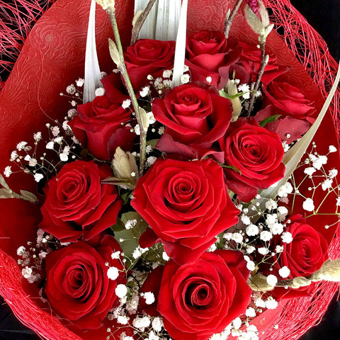 An absolute classic bouquet with a dozen beautifully wrapped red roses garnished with greenery and a light spray.